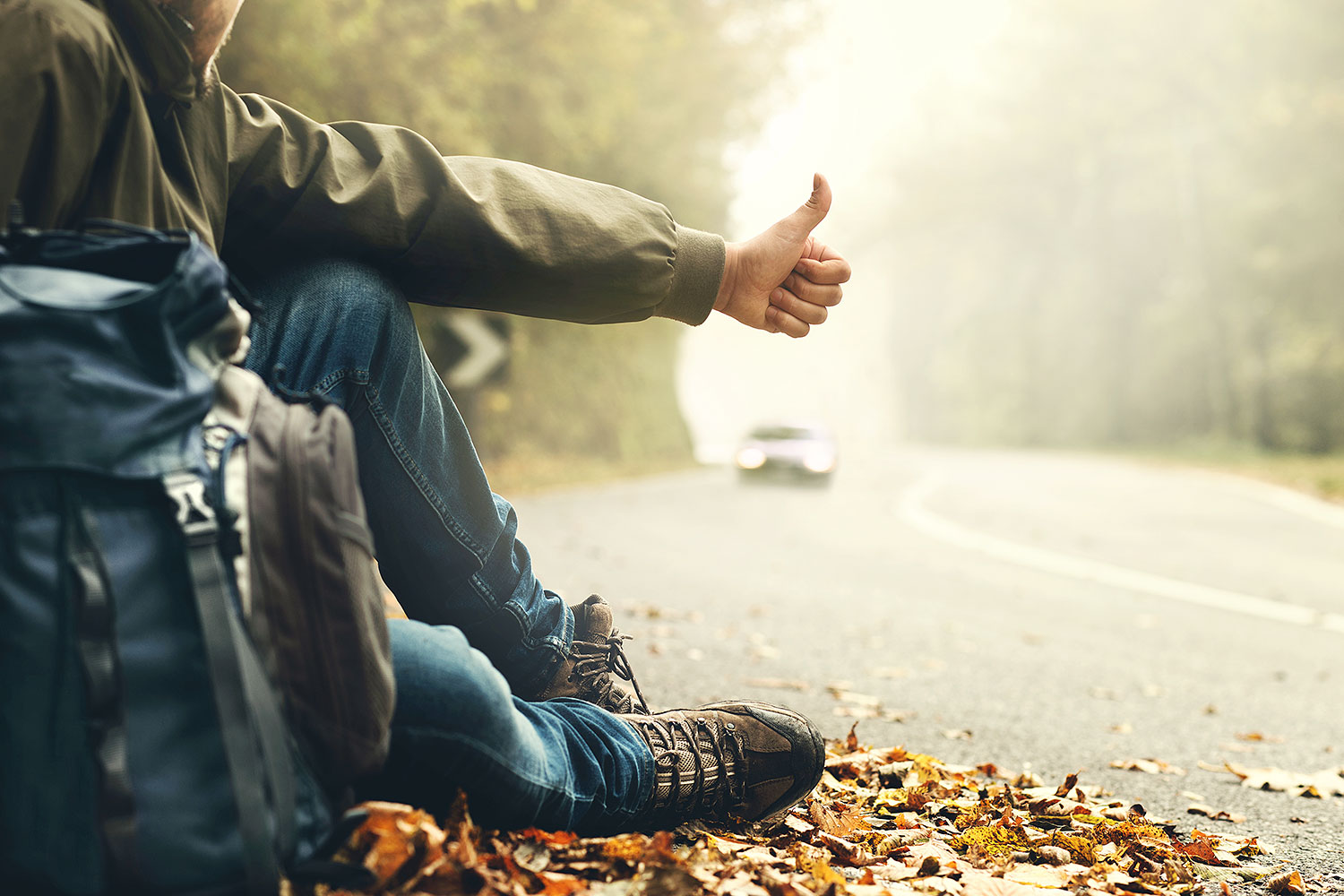 Man sitting on the road with backpack hitchhiking