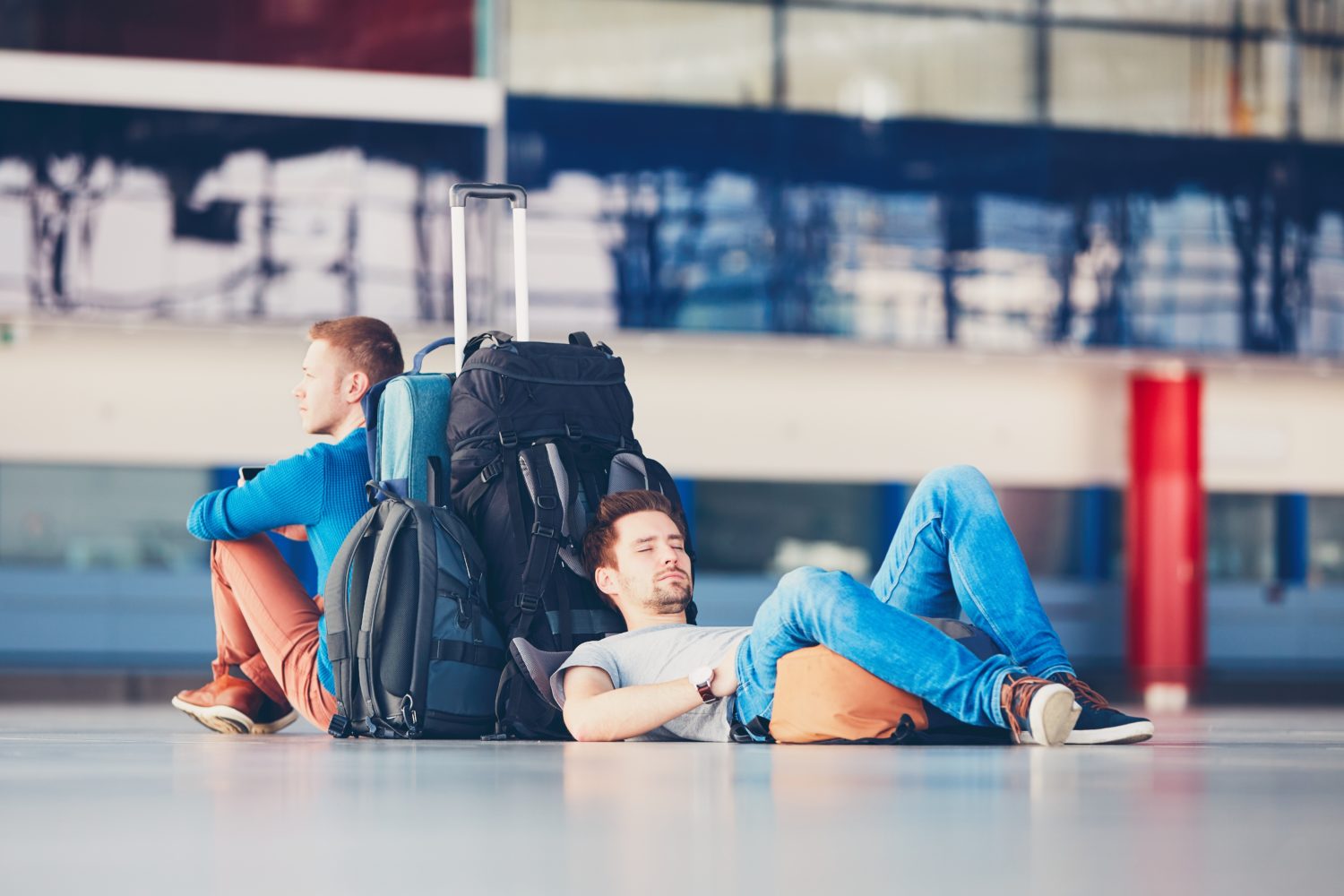 Two young men with bags are bored and resting while waiting at an airport for a plane from Prague to Berlin