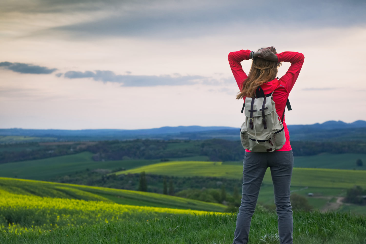 Young woman in red blazer with gray backpack looking at a view of Czech countryside while walking from Prague to Vienna