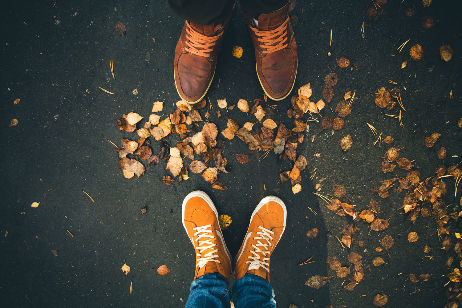 Two pairs of brown walking shoes on a ground with brown leaves