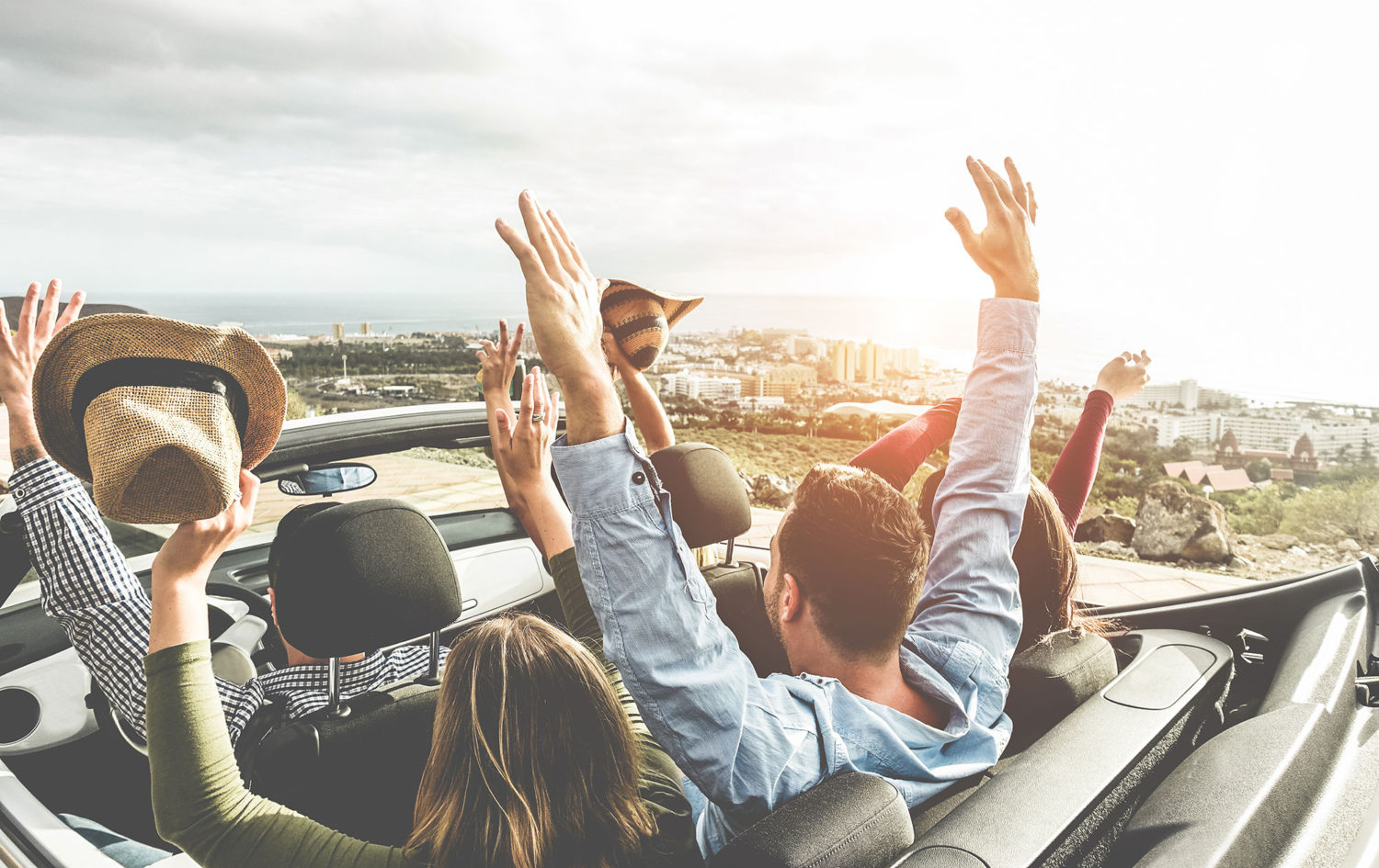 People waving hands in an open-top car while driving in Portugal countryside